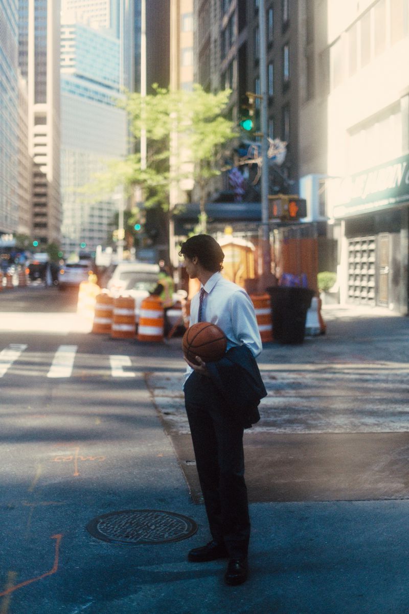 Model Mehdi Abouzaid holding a basketball on a city street wearing a light blue dress shirt, tie, and dark trousers.