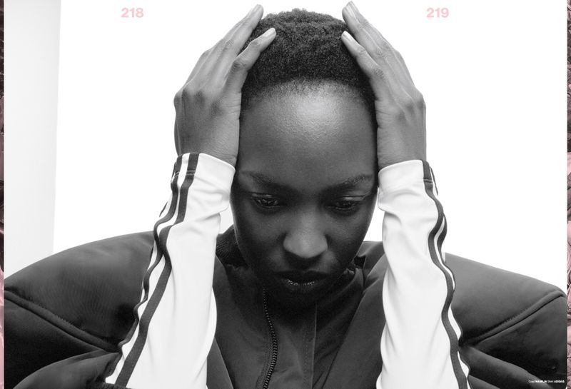 Black and white studio shot of an adult female with her hands on her head, wearing a jacket with athletic stripes on the sleeves.