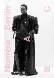 Model Nicole Atieno in a black oversized coat and sporty tracksuit against white seamless background for Numéro Berlin cover.