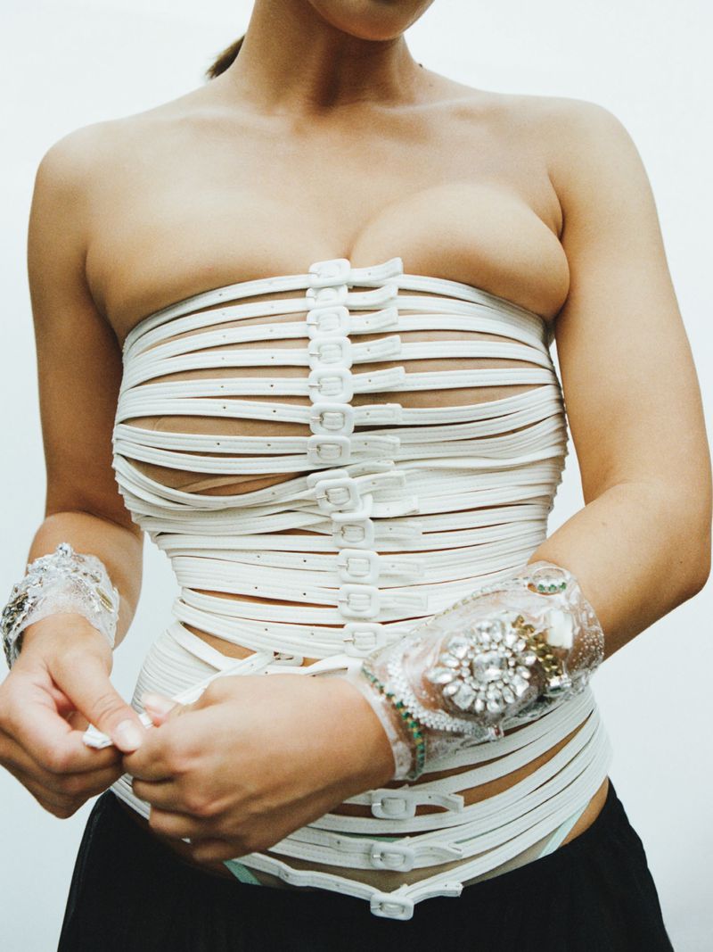 Model wearing a strapless white belted corset top with buckles down the center and jeweled crystal cuffs against a white backdrop.