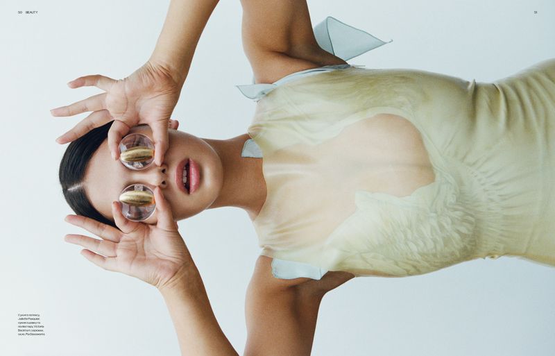 Model holding clear glass spheres over eyes wearing a pale green dress against a plain white background for Vogue Ukraine
