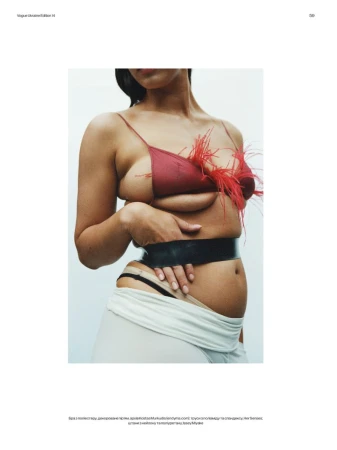 Model Noor Mutsaers posing in a red feathered bra top with black waist tape against a clean light studio backdrop for Vogue Ukraine.