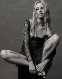 Model Maya Stepper sitting cross-legged wearing a sheer black lace dress for Vogue Adria
