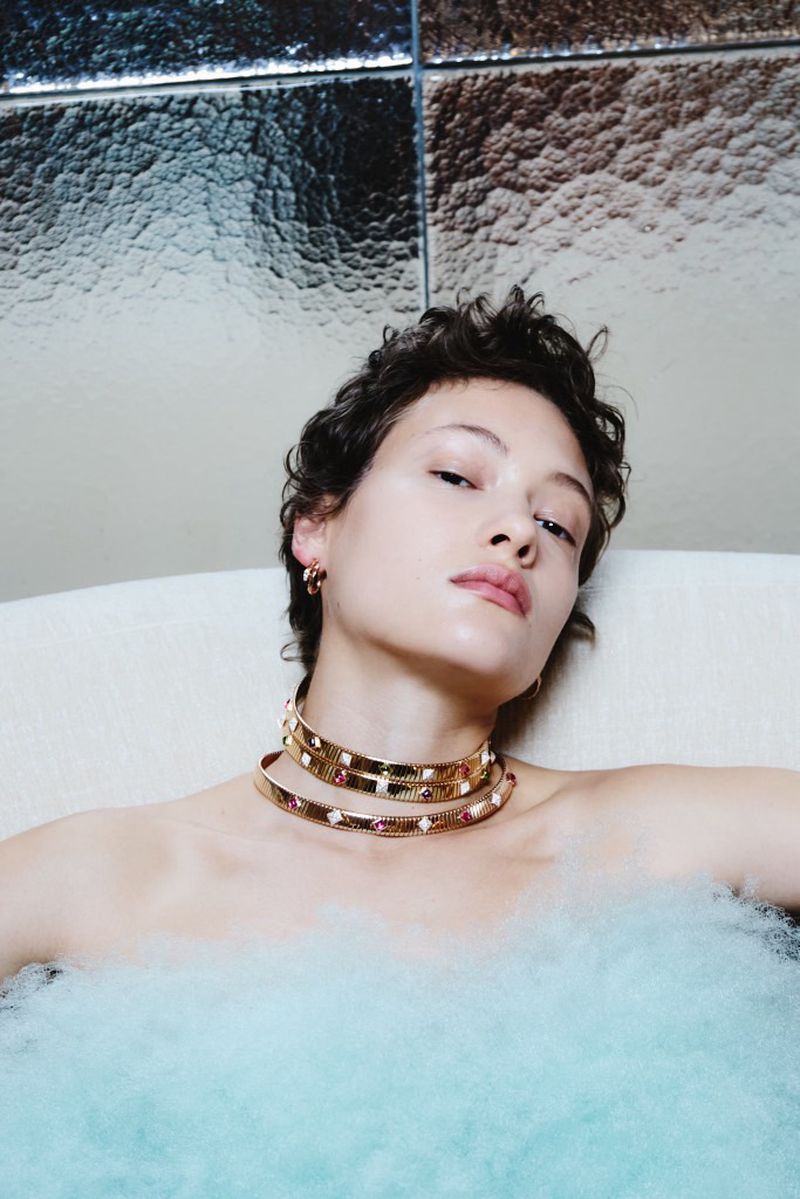 Woman in bathtub with water and gold jewelry. Close-up shot in an indoor setting, showcasing beauty and fashion.