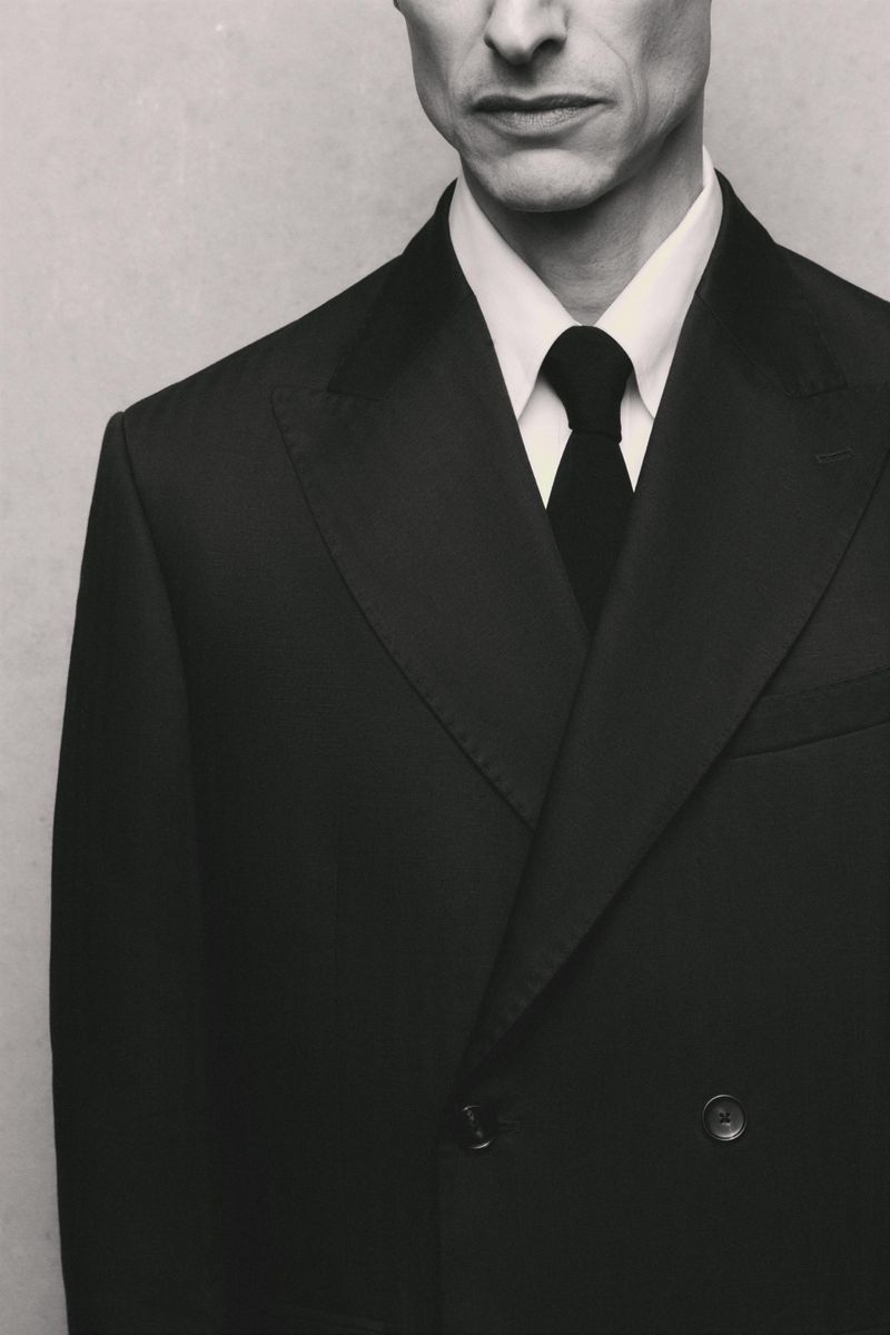 Close-up of model Jonas Mason wearing a black double-breasted suit jacket, white dress shirt, and black tie for Zara Suits Collection.