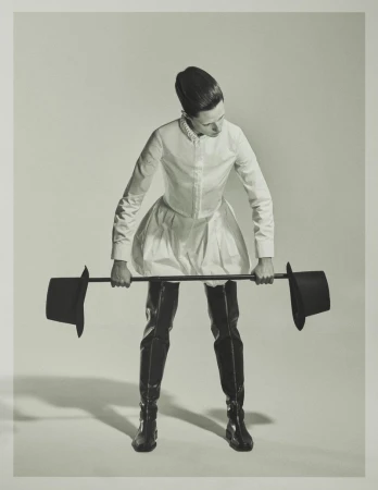 Julia Banas posing with a top hat barbell wearing a white balloon skirt and black thigh-high boots against a grey studio backdrop.