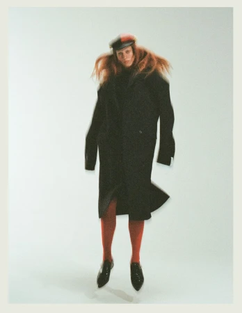 Model in long black coat and red tights jumping against a plain white background for Tidal Magazine