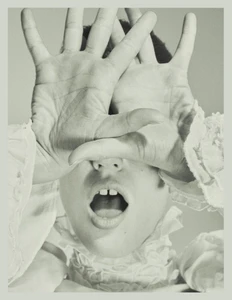 Julia Banas posing with open palms covering her eyes and mouth open wearing a white ruffled collar.
