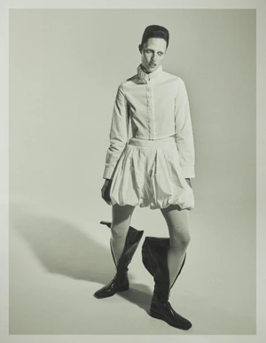 Model Julia Banas posing in a white button-down shirt, matching bubble shorts, and wide black boots against a studio backdrop.