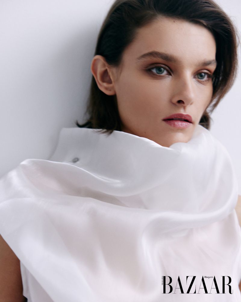 Close-up portrait of a woman with brown hair wearing a sheer white top against a white background, fashion photography.