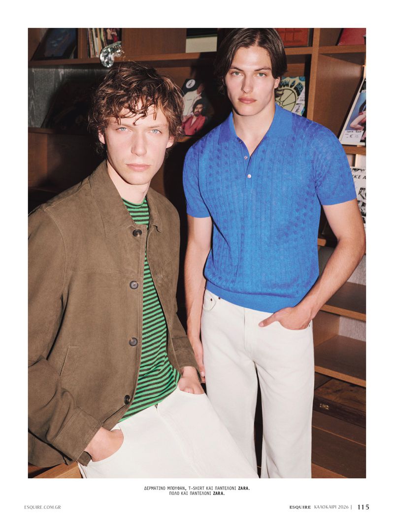 Two male models posing indoors, one in a brown jacket and green striped shirt, the other in a bright blue knit polo and white trousers.