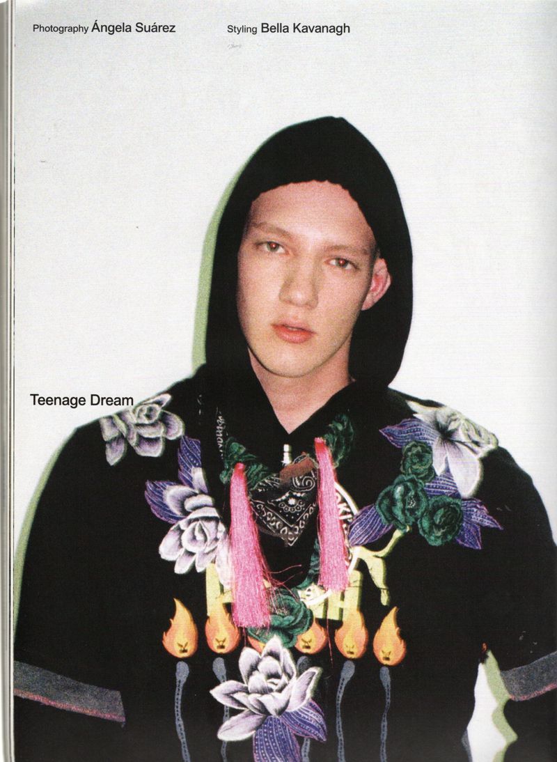 A young man wearing a black hooded sweatshirt with colorful floral embroidery and pink tassels against a light studio backdrop.
