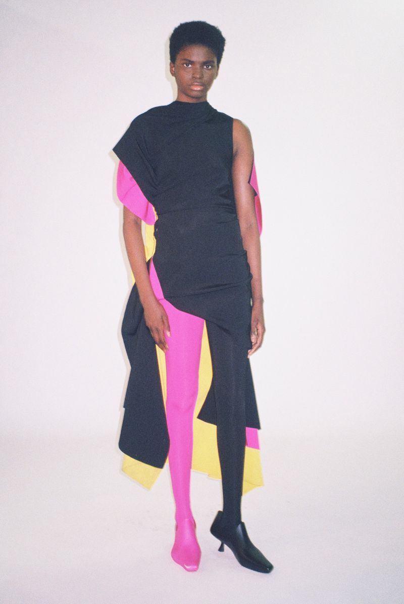 Model Rachel Agbonze in an asymmetrical black dress with mismatched pink and black tights against a white seamless background.