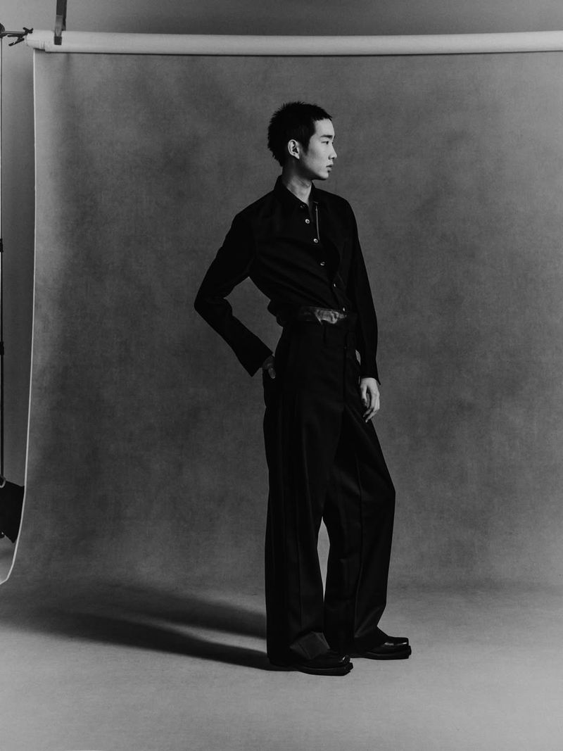 Man wearing a dark button-down shirt and trousers posing against a grey seamless studio backdrop