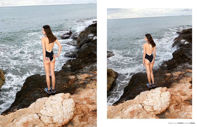 Model Sara Dijkink wearing a black backless swimsuit with white trim standing on rocky cliffs by the sea for Knack Weekend.