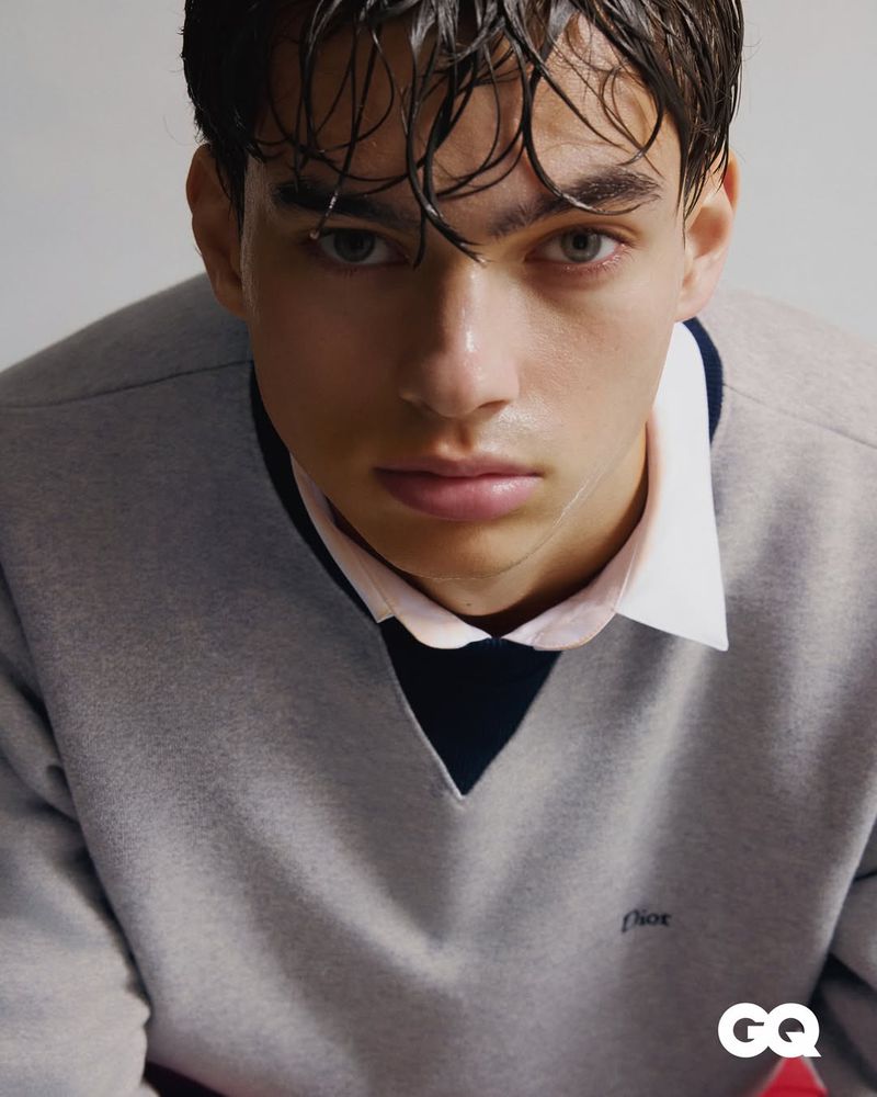 Close-up portrait of a man with wet hair wearing a grey Dior sweater over a collared shirt.