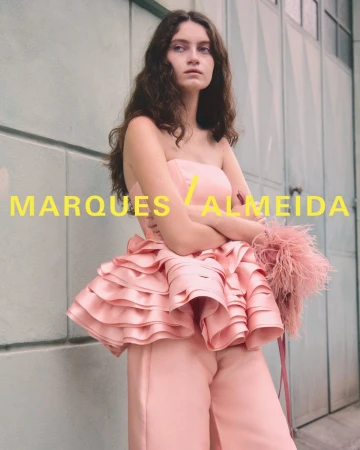 Model wearing a strapless pink ruffled peplum top and matching satin trousers against an industrial wall.