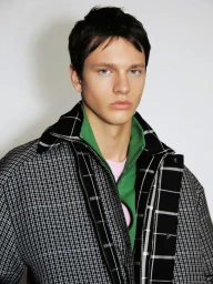 Male model wearing a layered black and white checked jacket over a green zip collar against a plain white background.