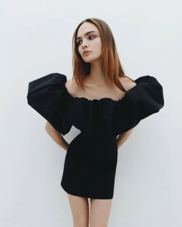 Model wearing a black off-the-shoulder mini dress with voluminous puff sleeves against a plain white studio background.