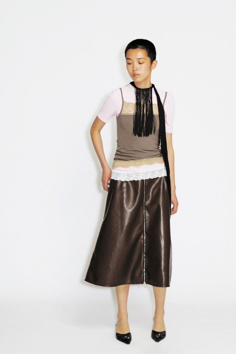 Model Echo Zhao in a layered lace camisole top and glossy brown midi skirt posing against a white studio backdrop.