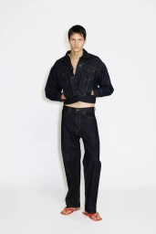 Male model wearing a dark raw denim cropped jacket and matching wide-leg jeans with red sandals against a white background.