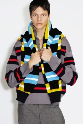 Model wearing a grey striped knit sweater with a blue and yellow striped knit draped over shoulders against a white background.