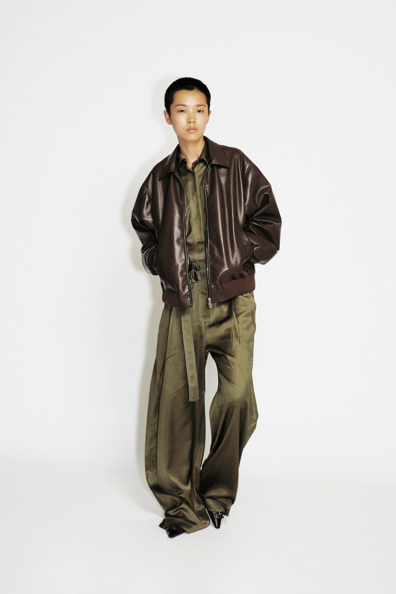 Model Echo Zhao wearing an oversized dark brown leather jacket and wide-leg olive green trousers on a white studio background.
