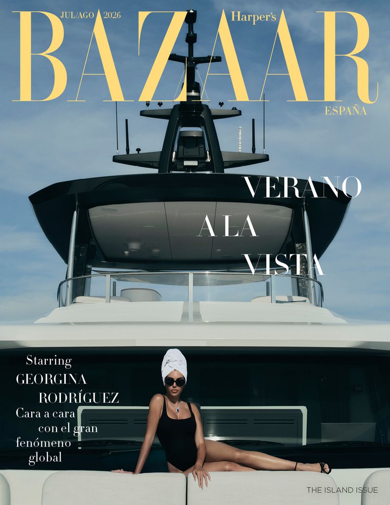 Georgina Rodríguez wearing a black swimsuit, white head towel, and sunglasses reclining on a yacht for Harper's Bazaar España.