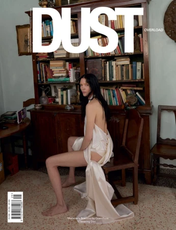 Mariacarla Boscono wearing a draped white silk backless gown seated on a wooden chair in front of a full bookshelf.