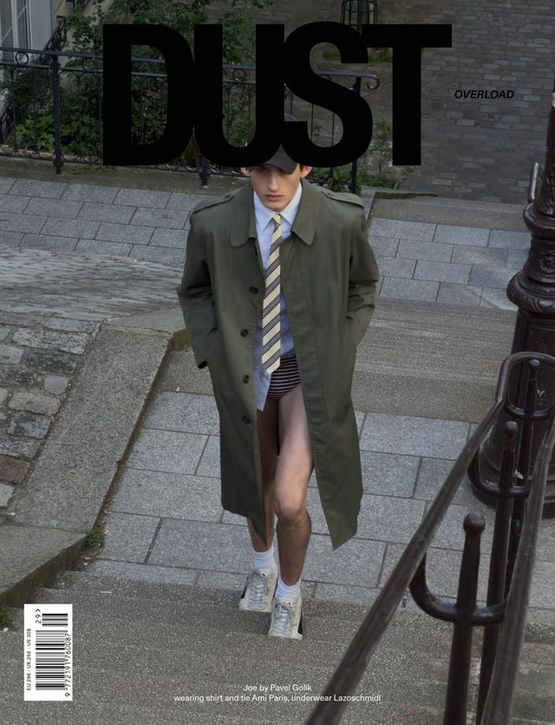 Model wearing an olive green trench coat and striped tie walking down stone outdoor steps.