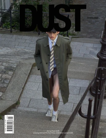 Model wearing an olive green trench coat and striped tie walking down stone outdoor steps.