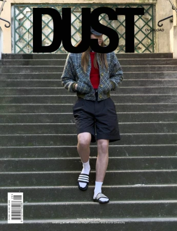 Model descending stone outdoor stairs wearing a plaid jacket, red top, black shorts, and slides for Dust Magazine.