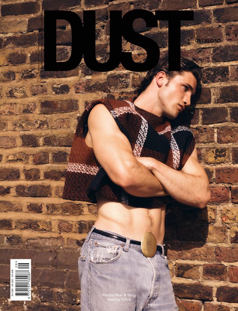 Model Max Knott posing in a cropped patterned knit vest and light wash jeans against an exposed brick wall for Dust Magazine.