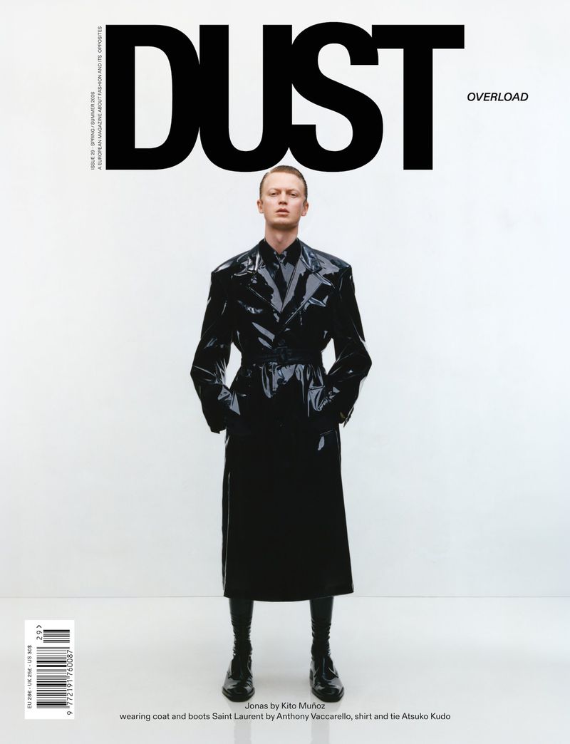 Model Charlie Jones wearing a glossy black trench coat and tie on the cover of Dust Magazine against a white background.