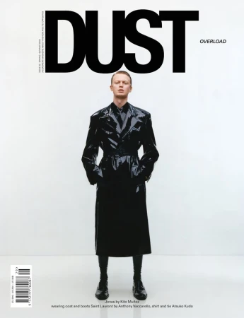 Model Charlie Jones wearing a glossy black trench coat and tie on the cover of Dust Magazine against a white background.