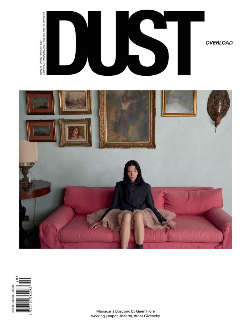 Model Mariacarla Boscono sitting on a pink sofa in a black jacket and ruffled skirt for the cover of Dust Magazine.