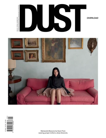 Model Mariacarla Boscono sitting on a pink sofa in a black jacket and ruffled skirt for the cover of Dust Magazine.