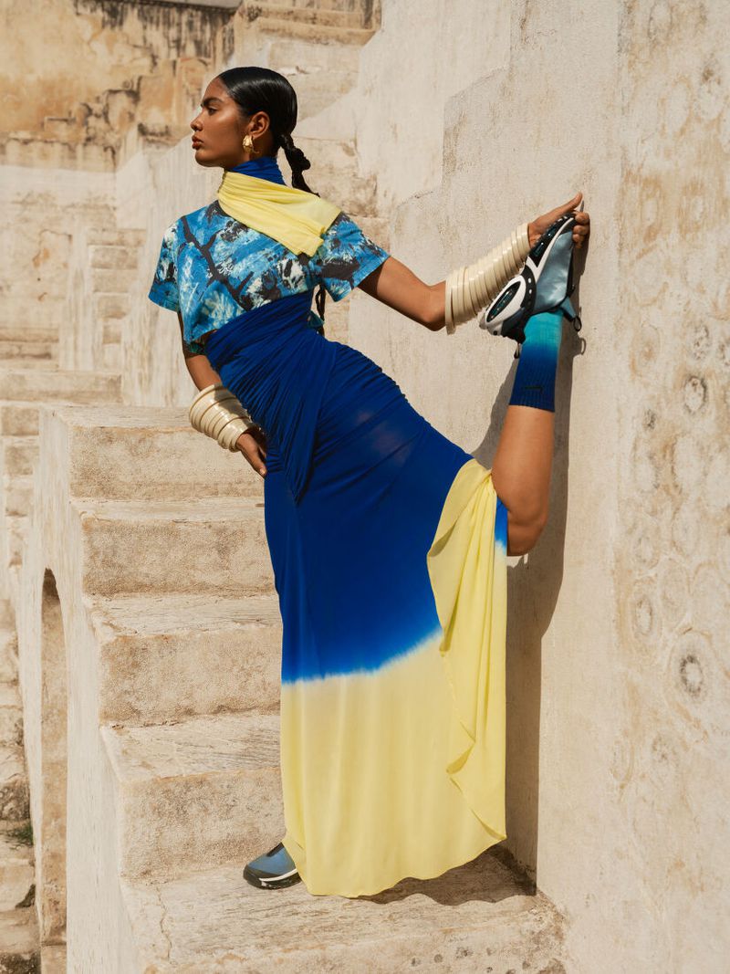 Fashion editorial shot of a woman in a tie-dye dress posing on stone steps, showcasing contemporary style in an outdoor setting.