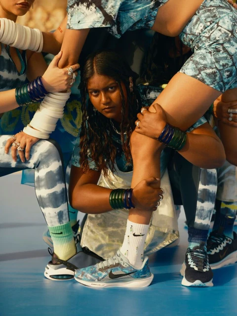 A group of diverse women posing in a close huddle wearing matching blue tie-dye inspired activewear and Nike athletic shoes in studio.