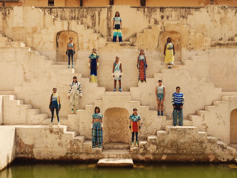 Fashion shoot with 12 young adults posing on the stairs of an ancient sandstone structure, wearing colorful clothing, outdoors in sunlight.