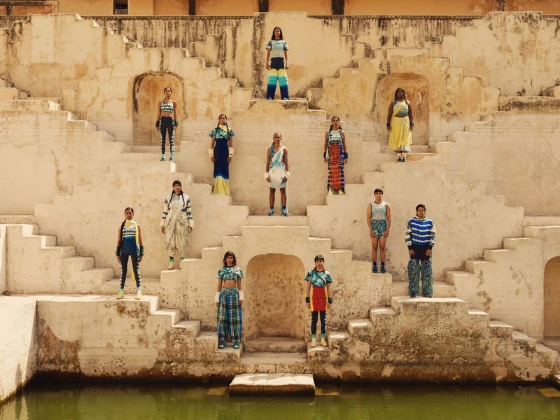 Fashion shoot with 12 young adults posing on the stairs of an ancient sandstone structure, wearing colorful clothing, outdoors in sunlight.
