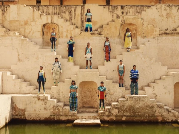 Fashion shoot with 12 young adults posing on the stairs of an ancient sandstone structure, wearing colorful clothing, outdoors in sunlight.