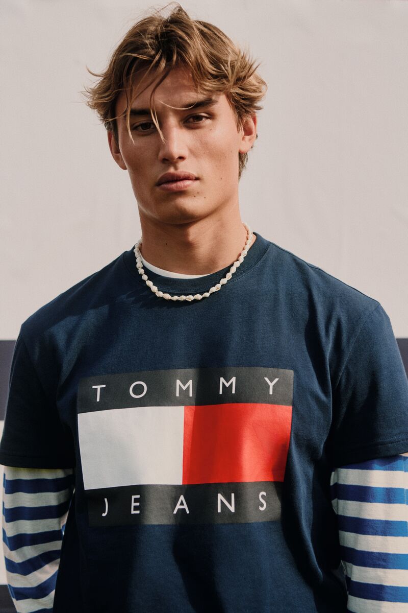 Model Joe Scott wearing a navy Tommy Jeans logo graphic t-shirt and white beaded necklace.