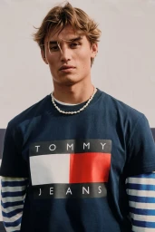 Model Joe Scott wearing a navy Tommy Jeans logo graphic t-shirt and white beaded necklace.