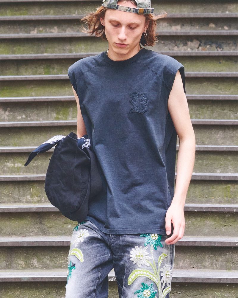 Young adult poses on stairs in dark t-shirt and jeans with floral embroidery. The outdoor image is medium shot and natural lighting.