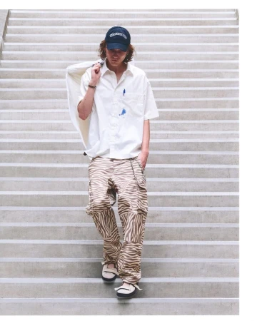 Model in zebra-print cargo pants and white short-sleeve button-down shirt walking down concrete stairs