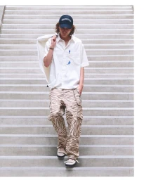 Model in zebra-print cargo pants and white short-sleeve button-down shirt walking down concrete stairs