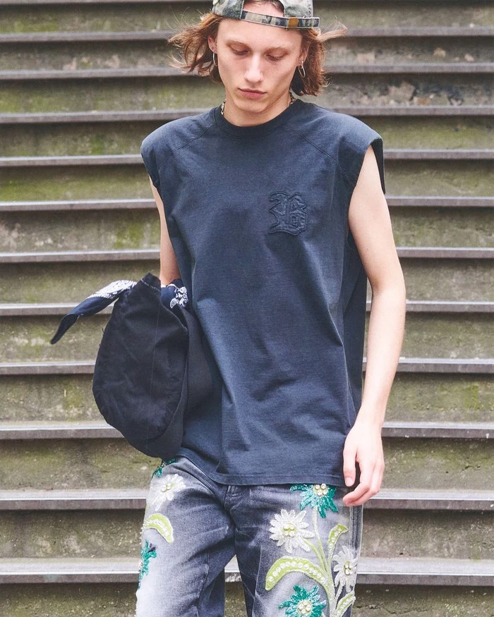 Model wearing a dark sleeveless t-shirt and floral embroidered jeans standing on outdoor stone steps