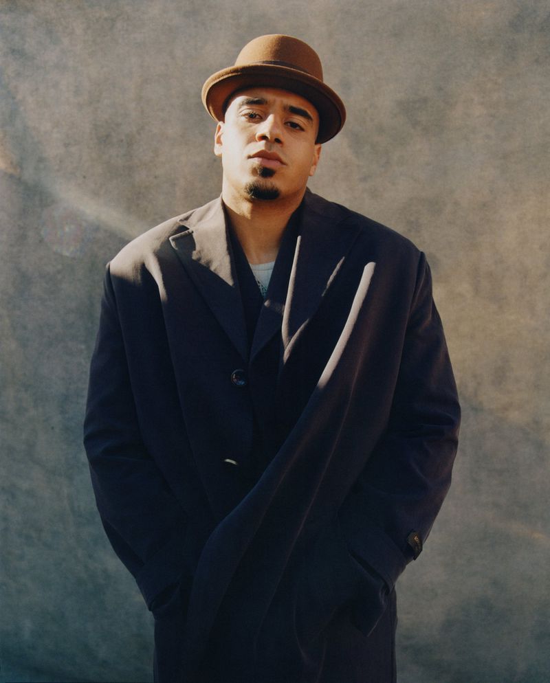 Man wearing a dark coat and brown bowler hat posing against a mottled textured grey background for 72 Magazine