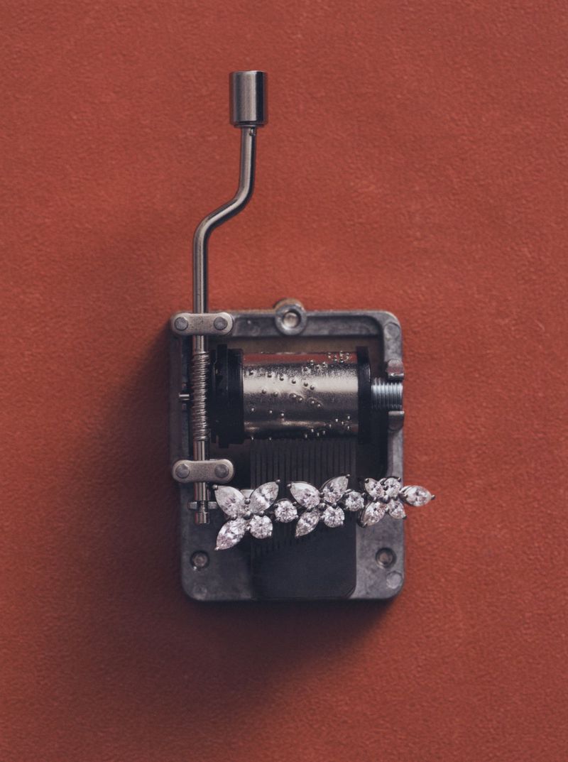 Diamond butterfly jewellery resting on a metal hand-crank music box mechanism against a terracotta background.